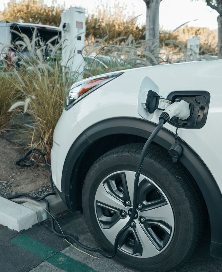A white electric vehicle plugged in and charging beside a planted verge