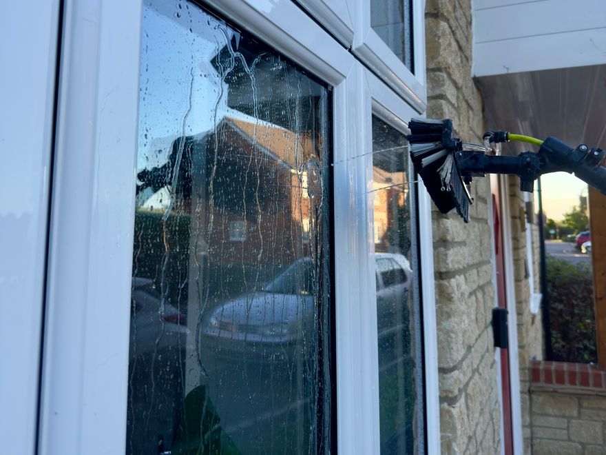 A water-fed brush head rinsing purified water down a window, the glass already running clear